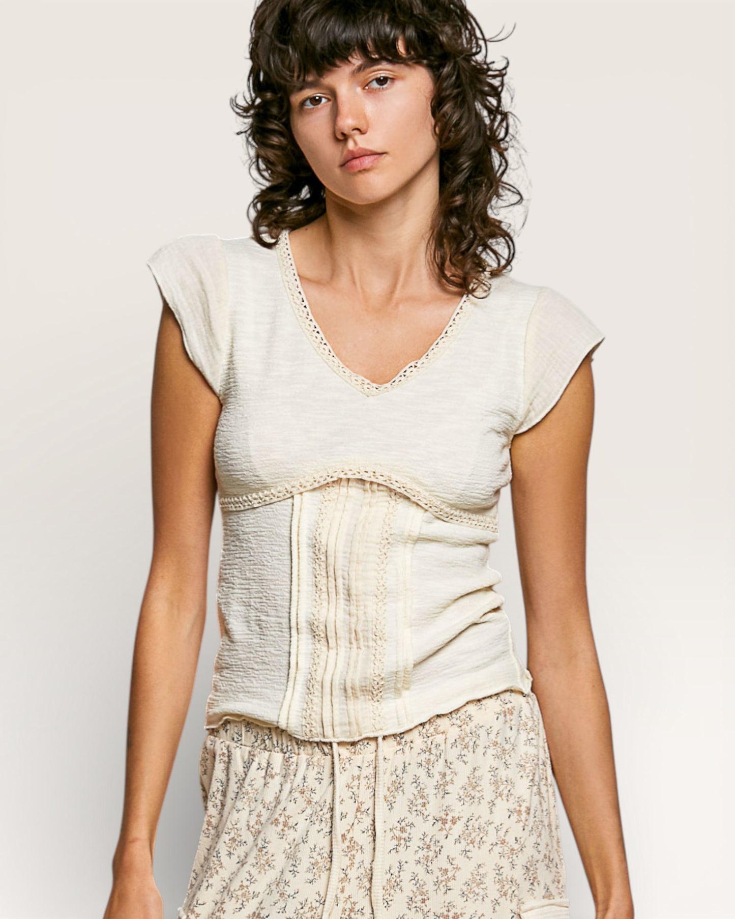 Woman wearing a light-colored top with lace details on a plain background