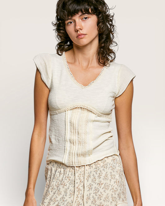 Woman wearing a light-colored top with lace details on a plain background