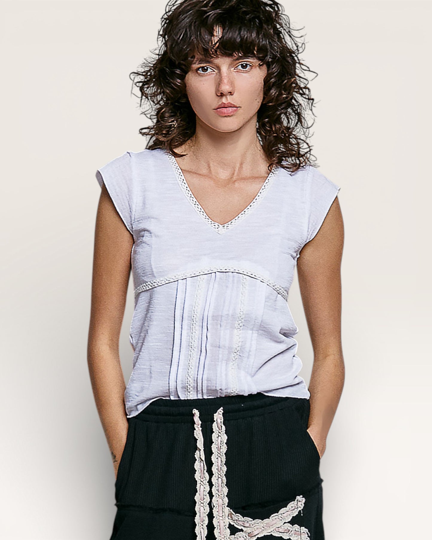 Woman wearing a light blue sleeveless top with lace details against a plain background
