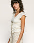 Woman wearing a light-colored sleeveless top with a plain background