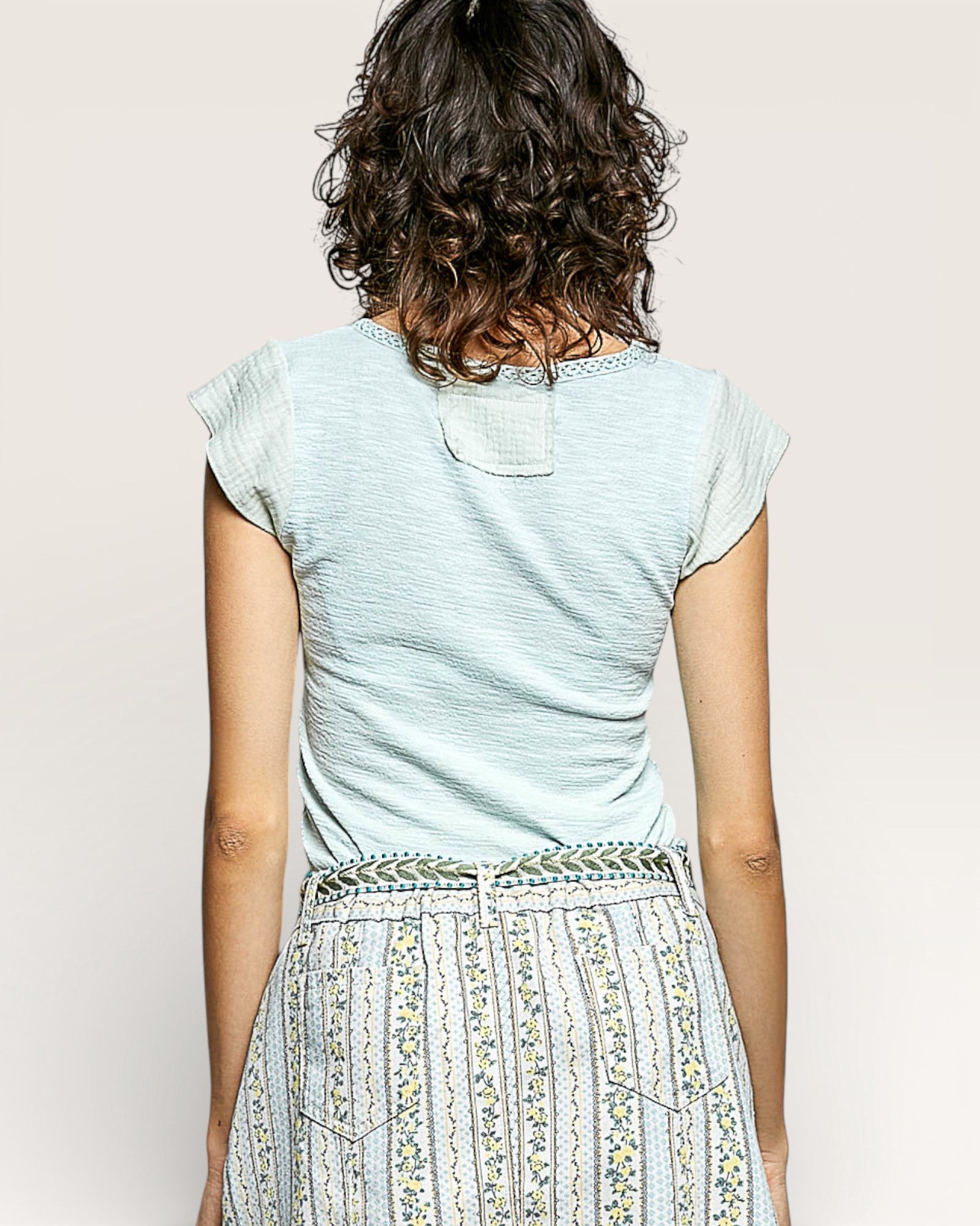 Person wearing a light blue top and patterned skirt against a plain background