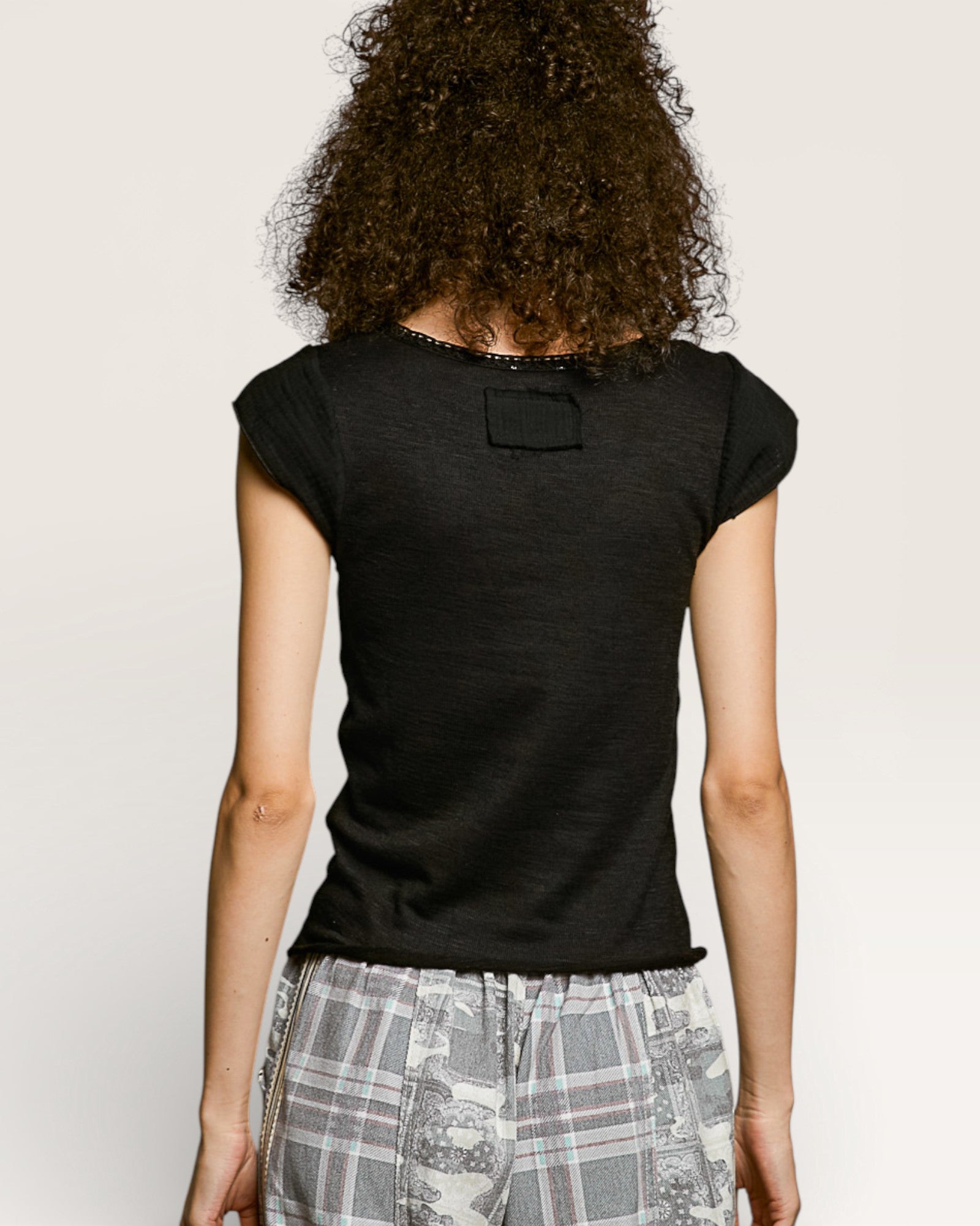 Person wearing a black t-shirt with a small patch on the back, standing against a plain background.