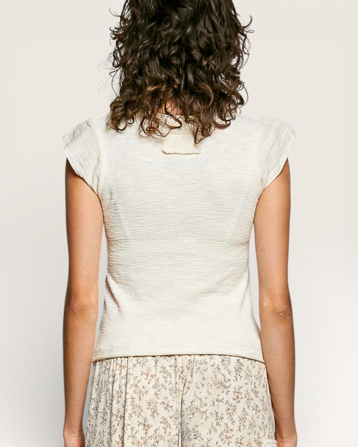 Person wearing a light-colored top with a plain background