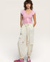 Woman wearing a pink top and white pants with floral details on a plain background
