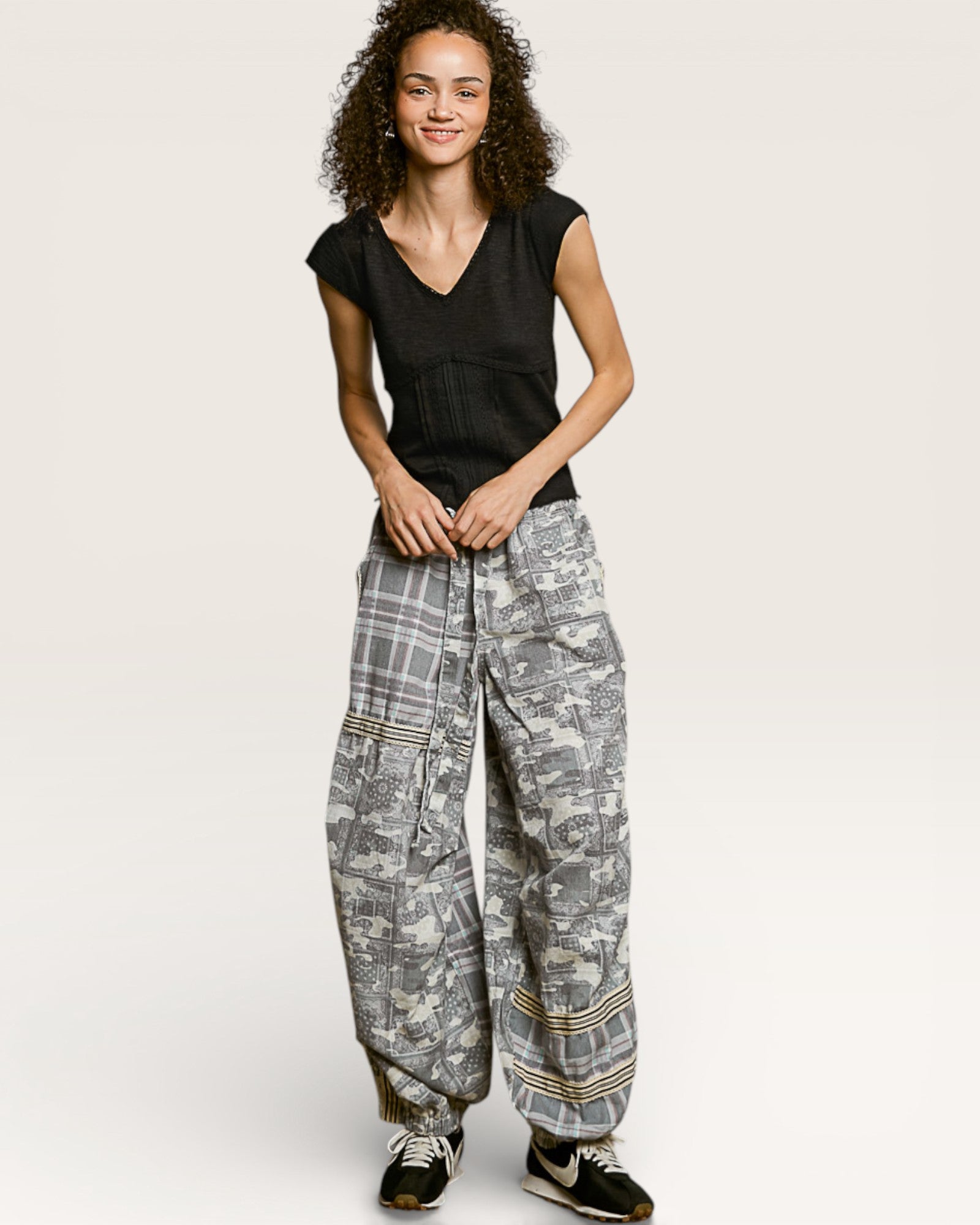 Person wearing a black top and patterned gray pants on a white background