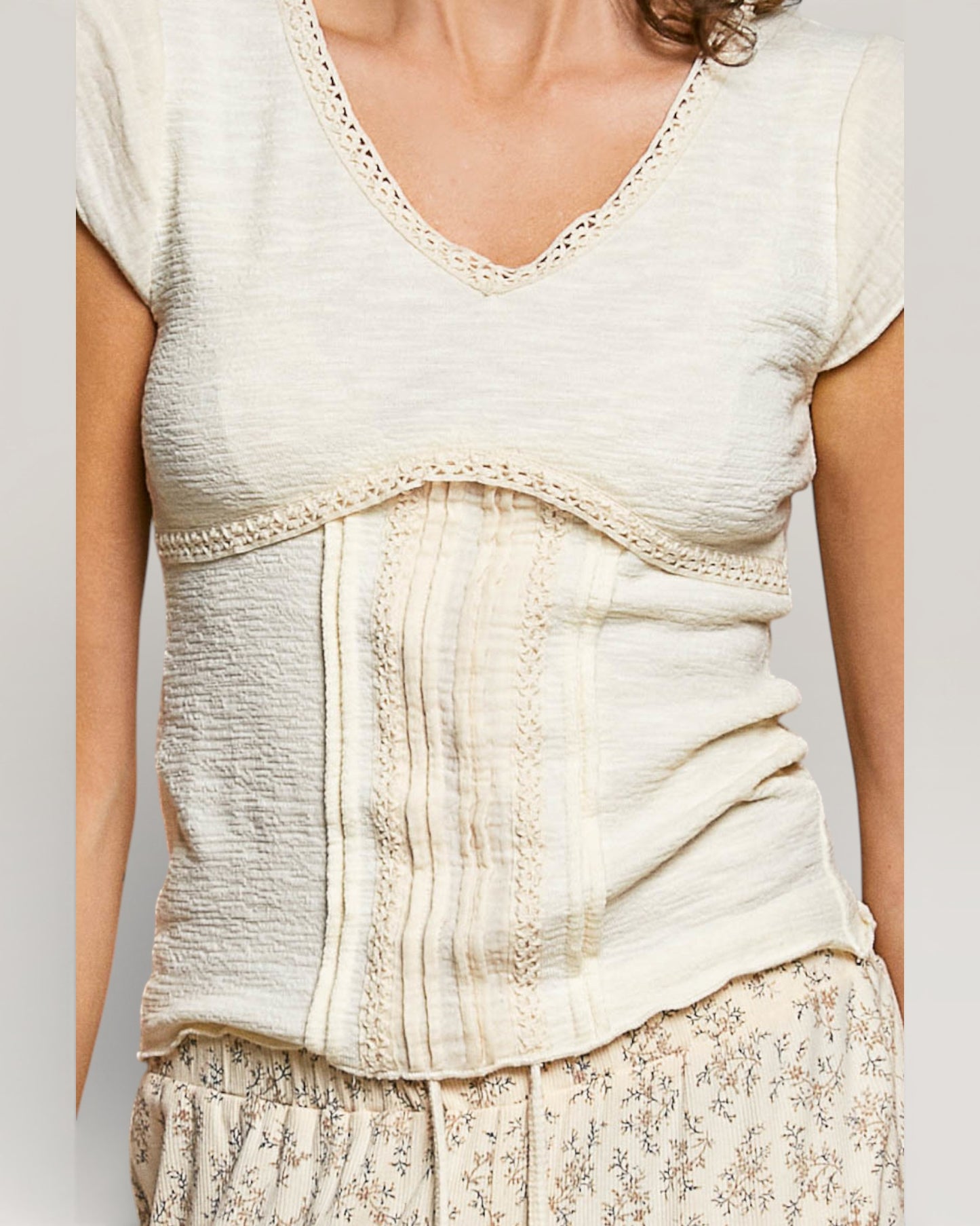Woman wearing a light-colored top with lace details on a plain background