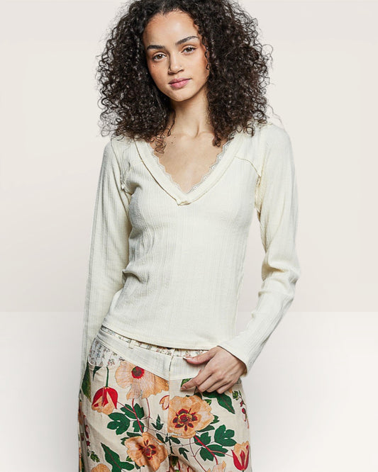 Woman wearing a white blouse and floral pants against a plain background