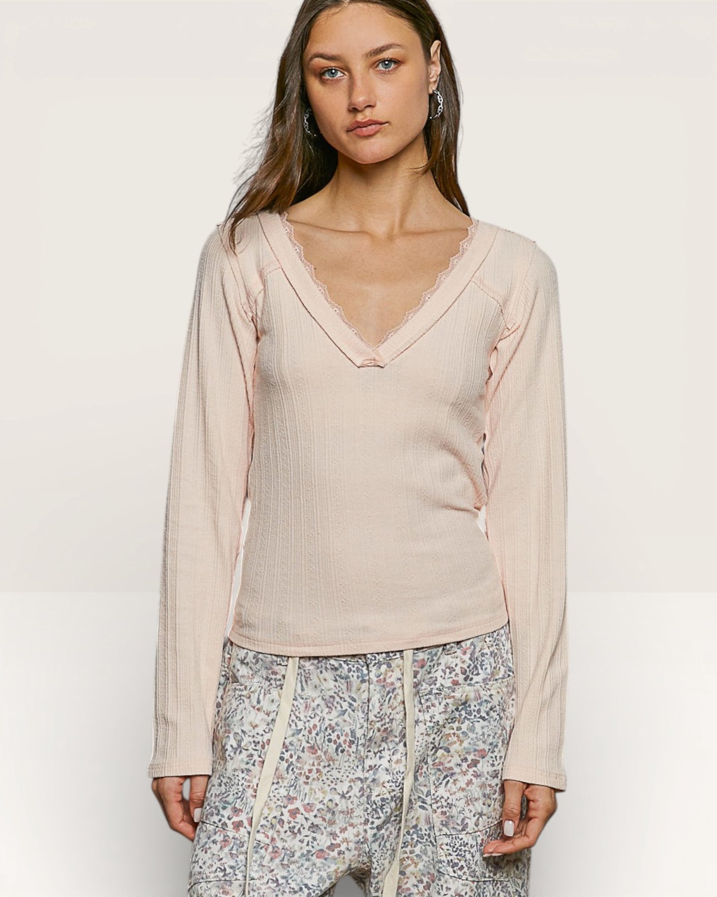 Woman wearing a beige long-sleeve top with floral pants on a white background
