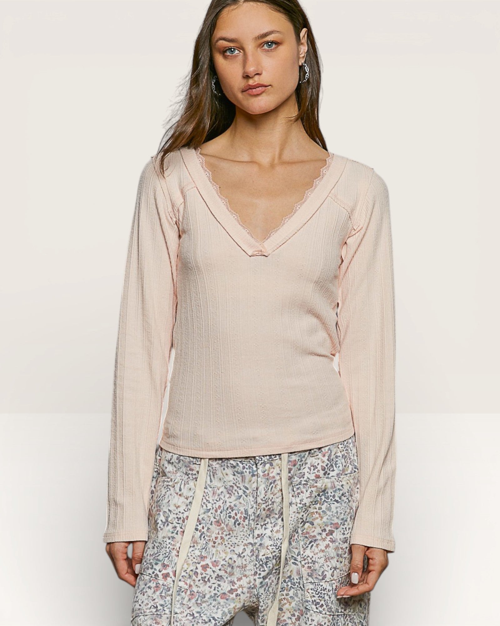Woman wearing a beige long-sleeve top with floral pants on a white background