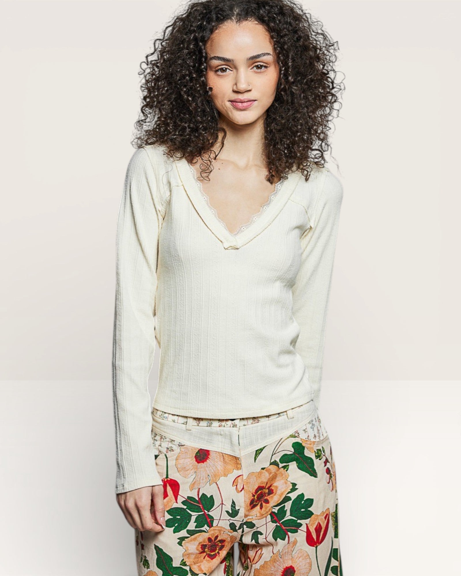 Woman wearing a light green sweater and floral pants on a plain background