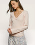 Woman wearing a light pink long-sleeve top with a subtle pattern on a plain background