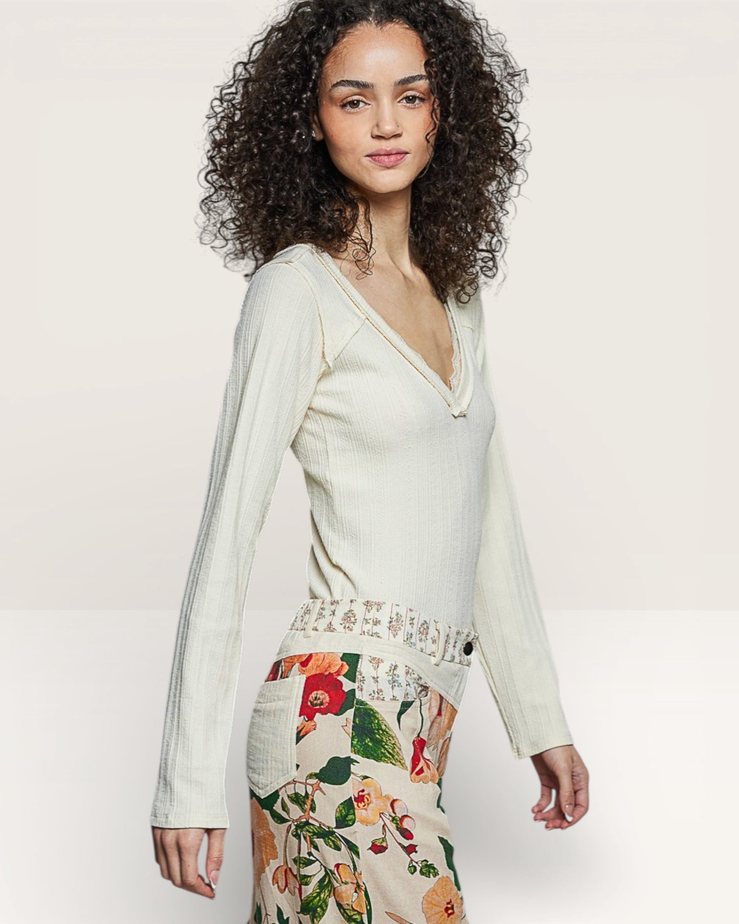 Woman wearing a light green long-sleeve top and floral skirt on a white background