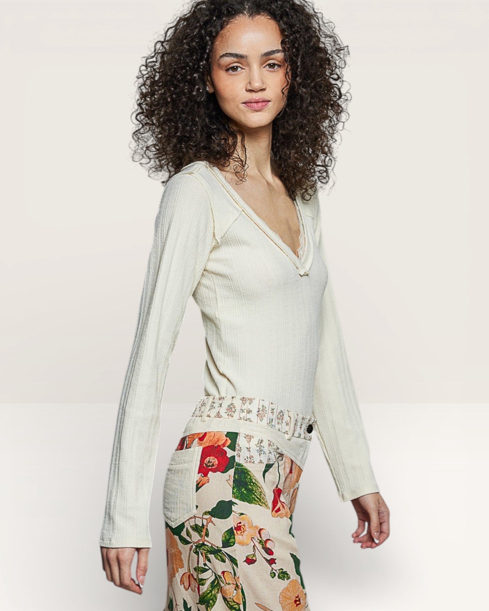 Woman wearing a light green long-sleeve top and floral skirt on a white background