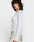 Woman wearing a light gray long-sleeve top with a plain background