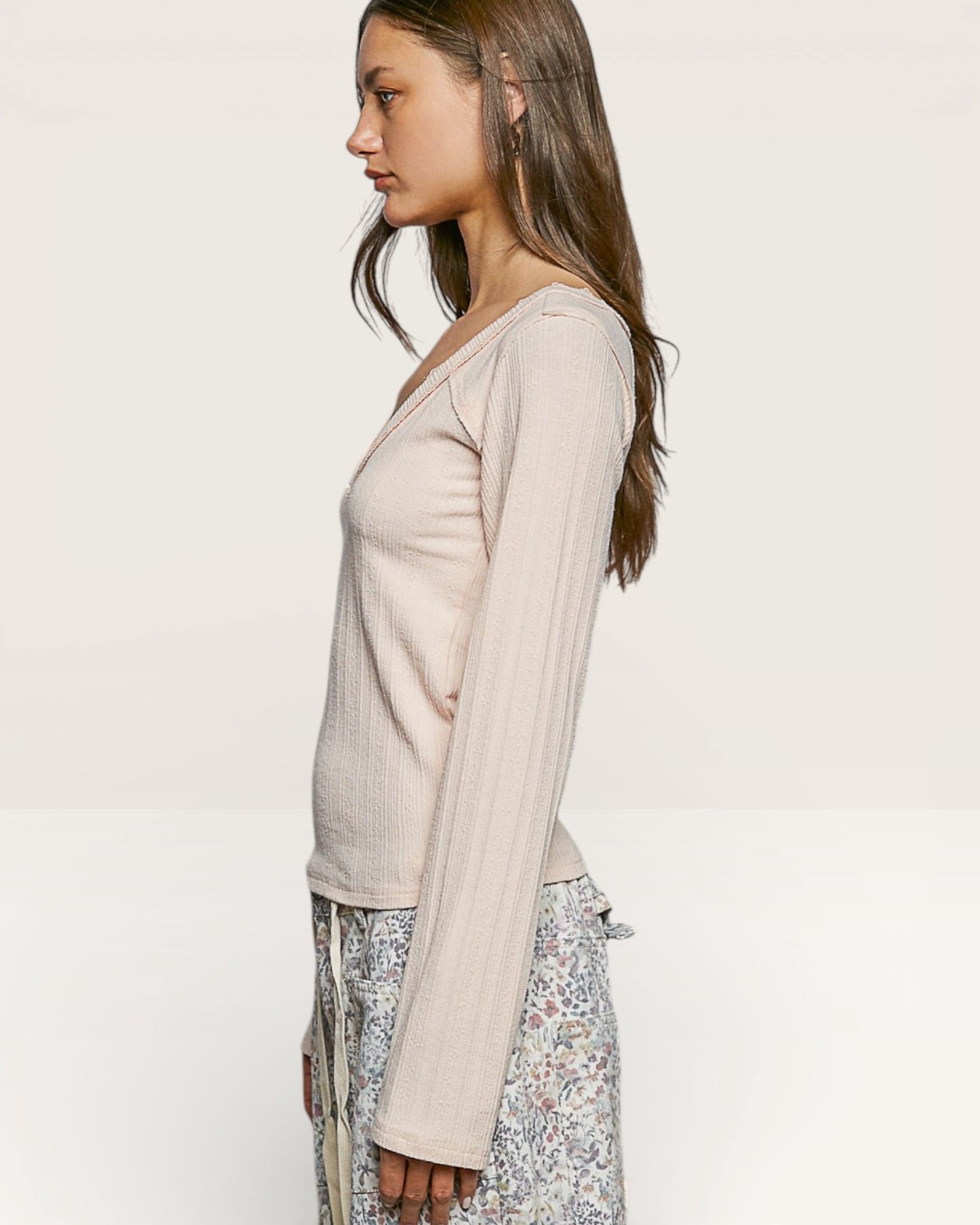 Woman wearing a beige long-sleeve top and floral skirt on a white background