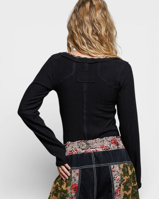 Person wearing a black long-sleeve top with floral and patchwork design on a white background