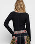Person wearing a black long-sleeve top with floral and patchwork design on a white background