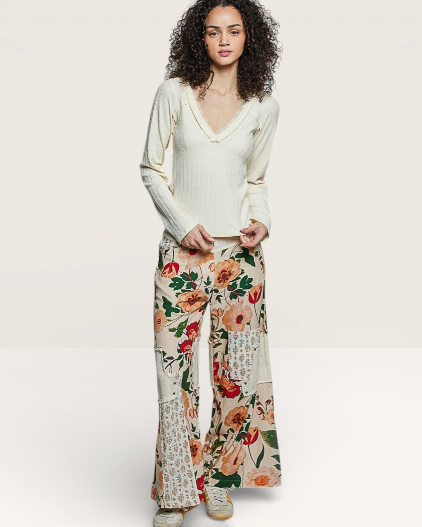 Woman wearing a white top and floral pants on a plain background