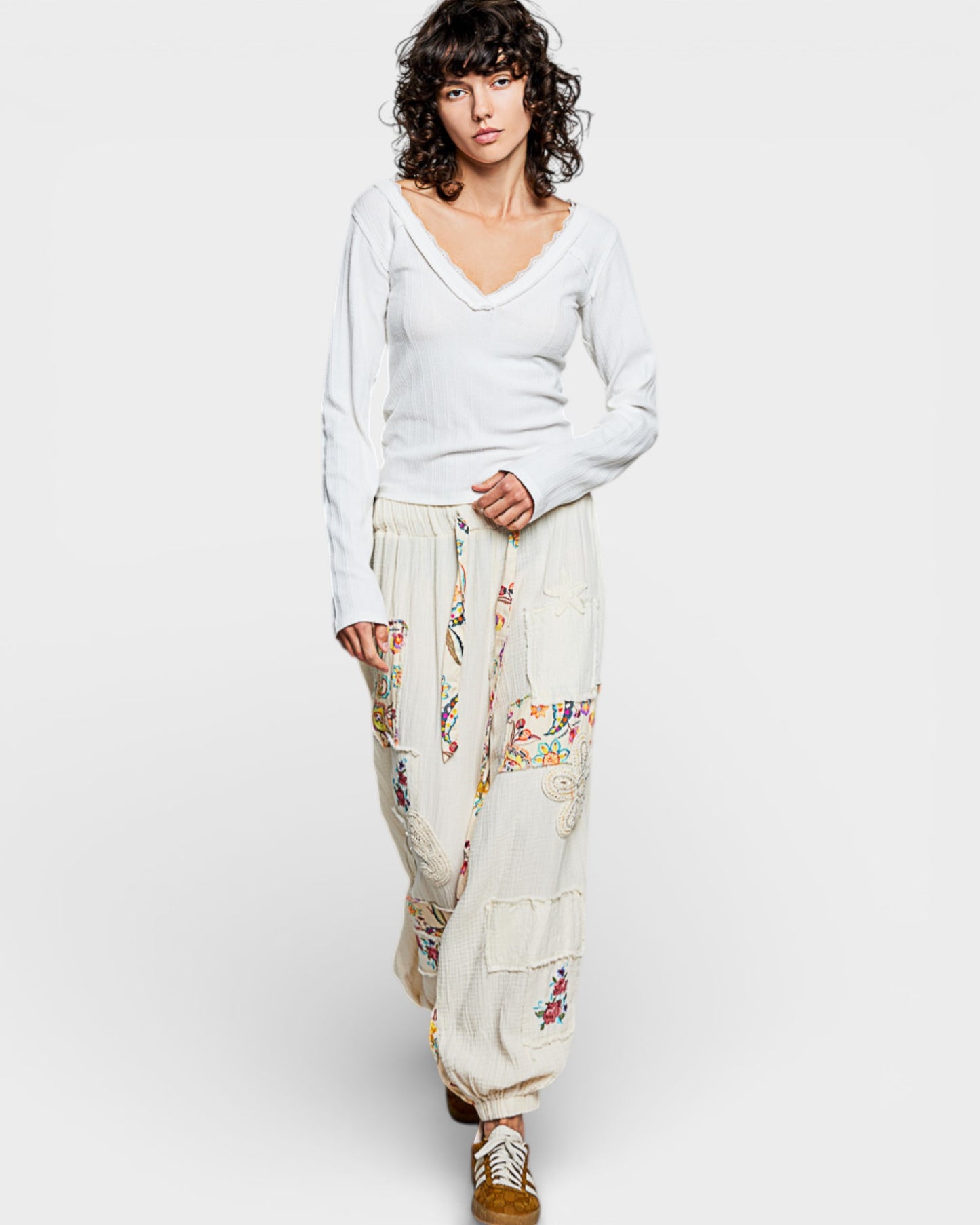 Woman wearing a white sweater and floral pants on a plain background