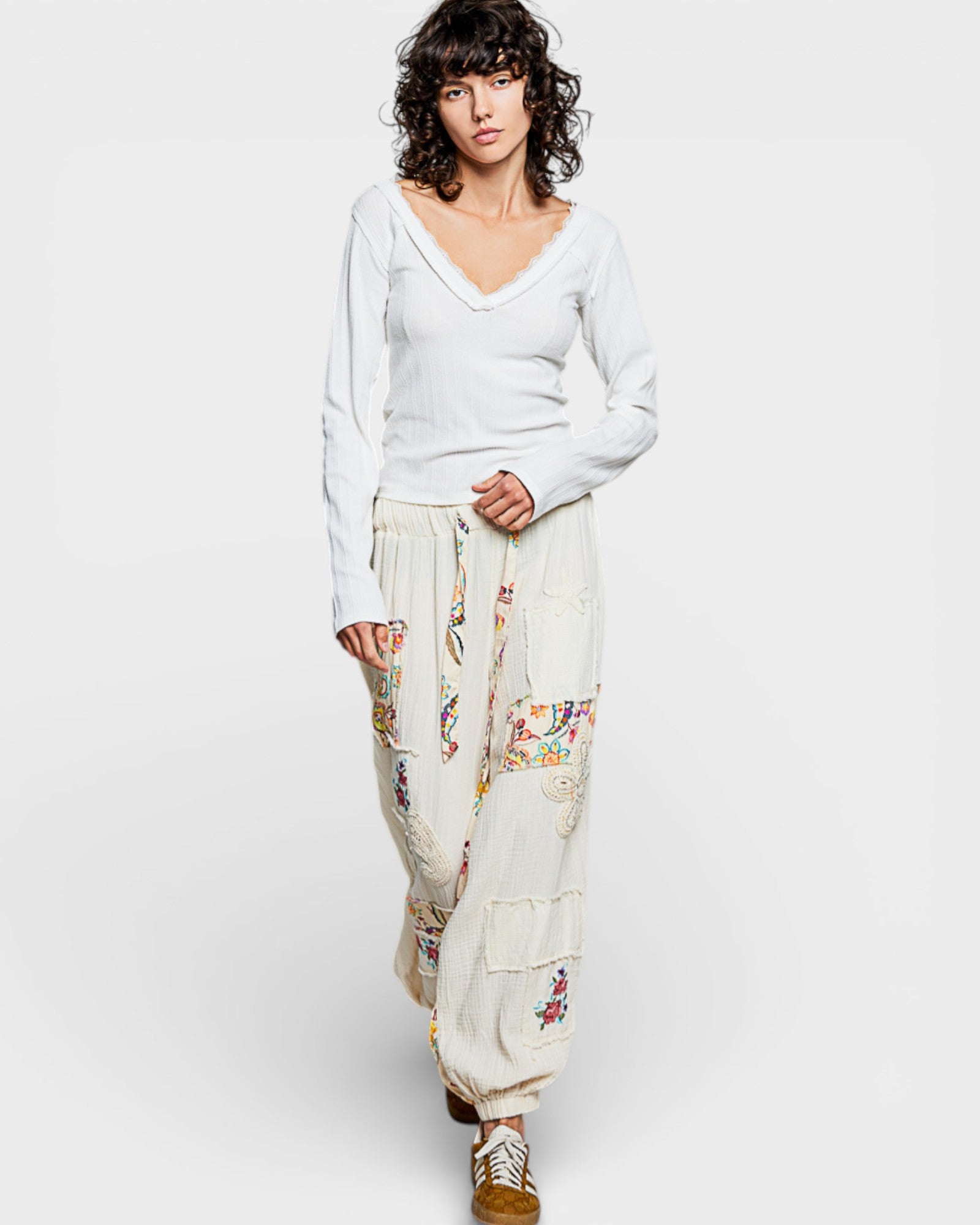 Woman wearing a white sweater and floral pants on a plain background