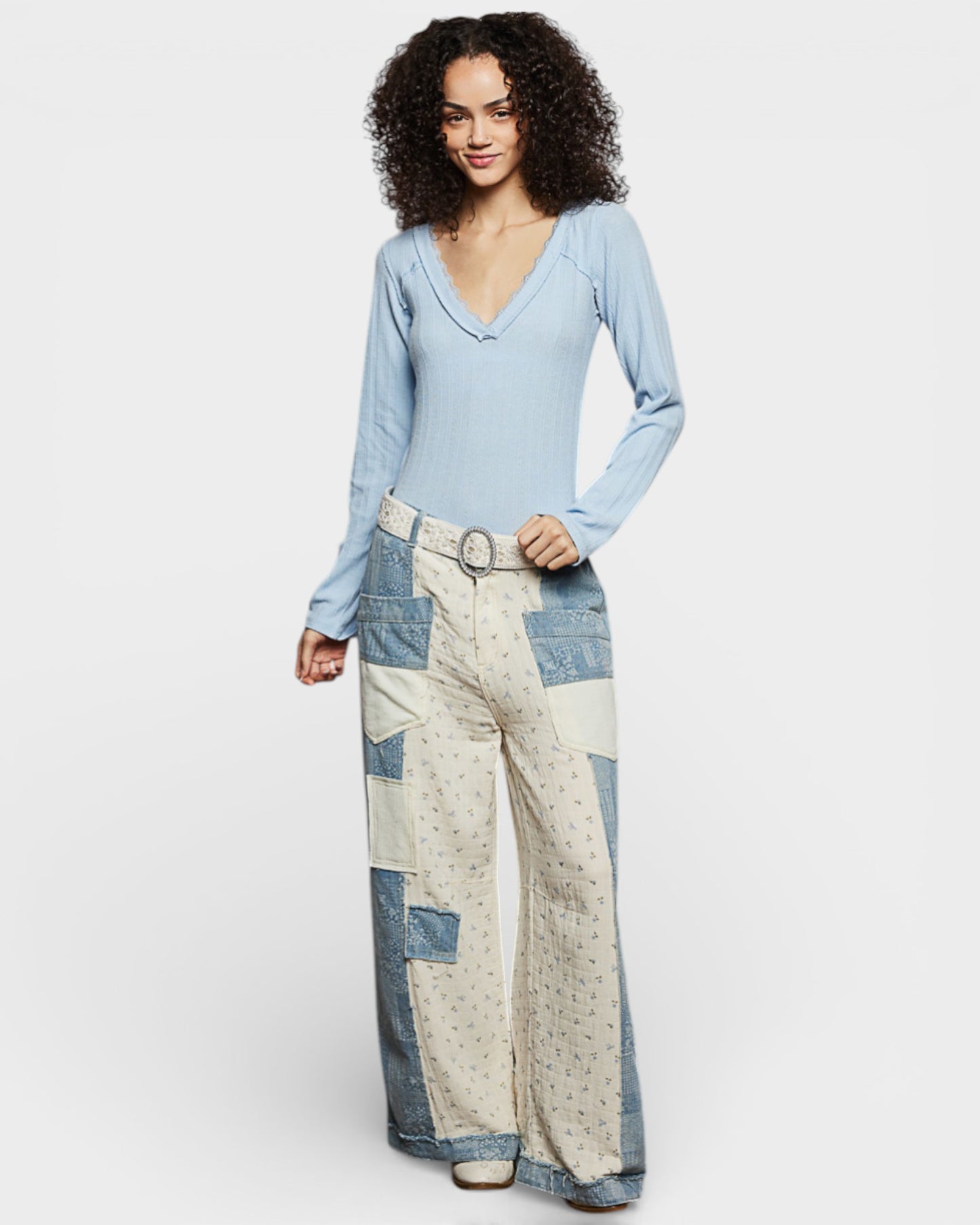Woman wearing a light blue long-sleeve top and patchwork pants on a white background