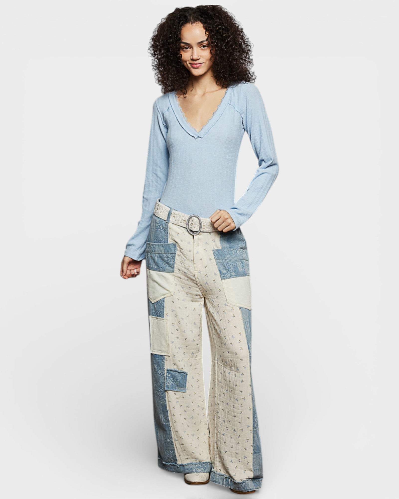 Woman wearing a light blue long-sleeve top and patchwork pants on a white background