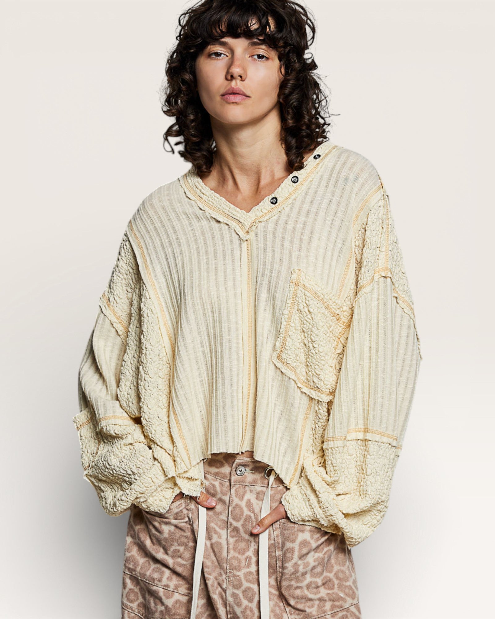 Person wearing a loose-fitting, cream-colored cardigan over a light shirt with leopard print pants on a plain background.