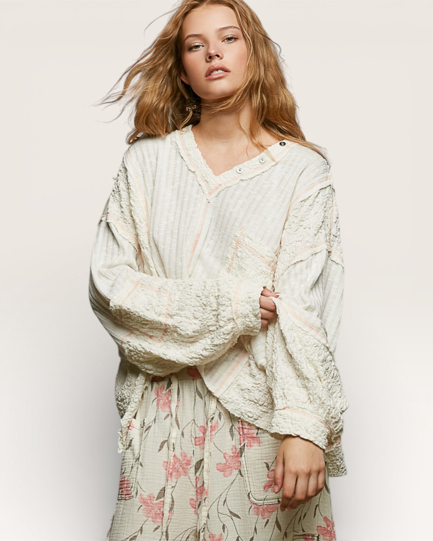 Woman wearing a textured white top over a floral dress on a plain background