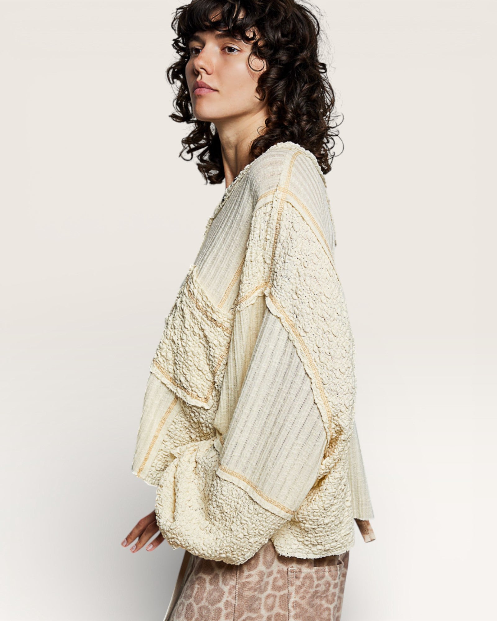 Woman wearing a textured beige shawl over a patterned dress on a plain background