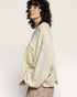 Woman wearing a textured beige shawl over a patterned dress on a plain background
