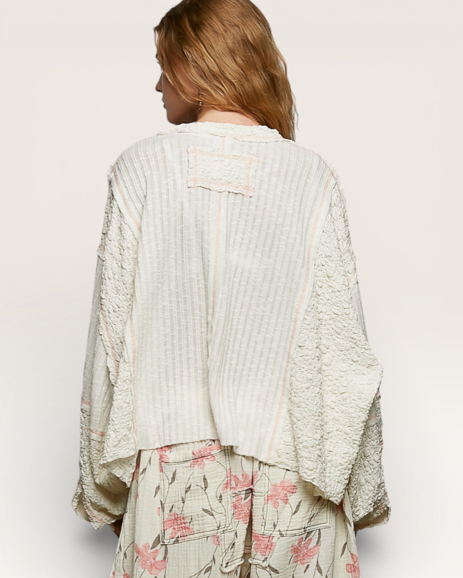 Woman wearing a textured white top and floral skirt on a plain background