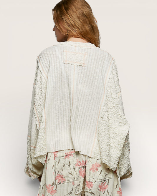 Woman wearing a textured white top and floral skirt on a plain background