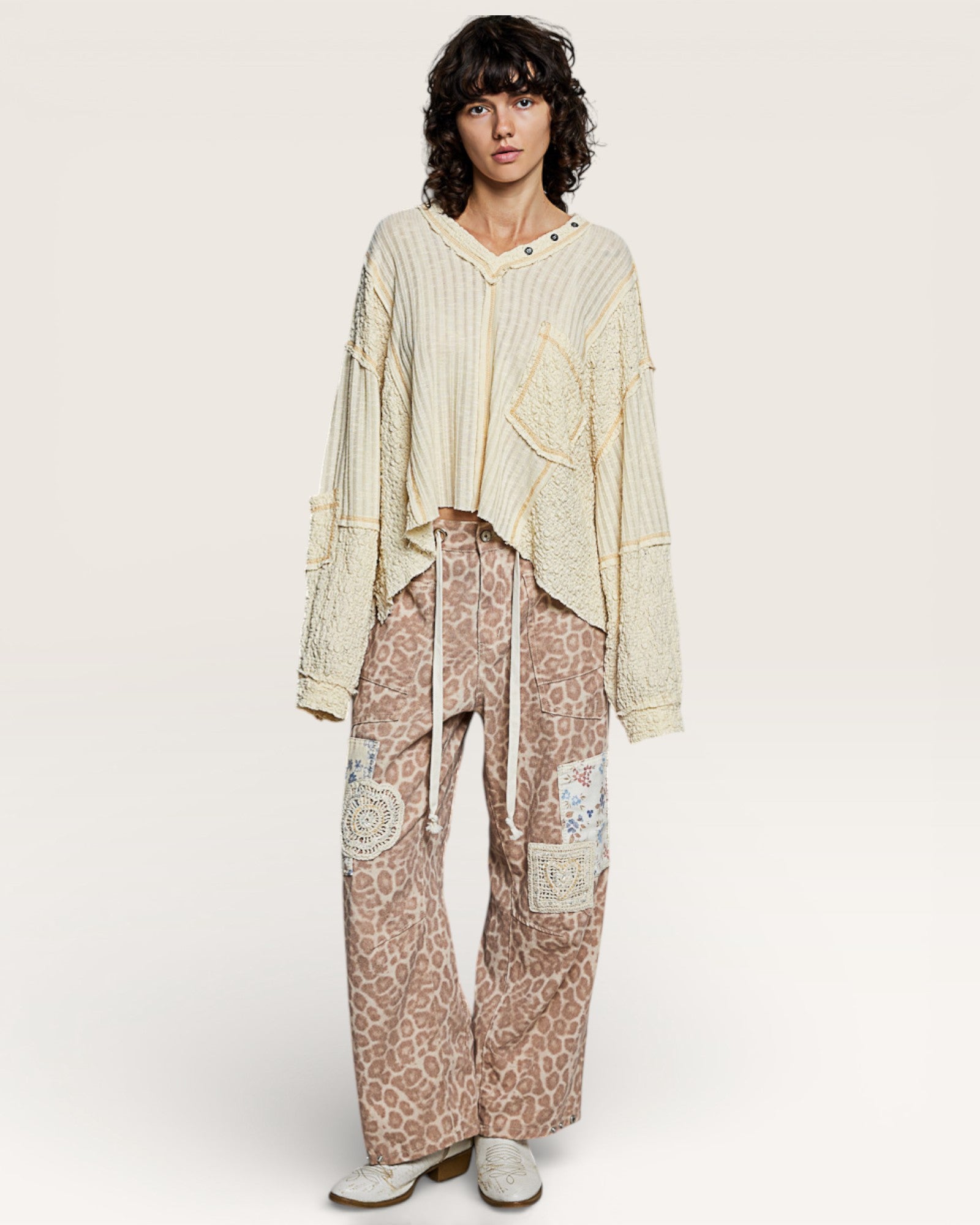 Person wearing a light-colored sweater and leopard print pants on a white background