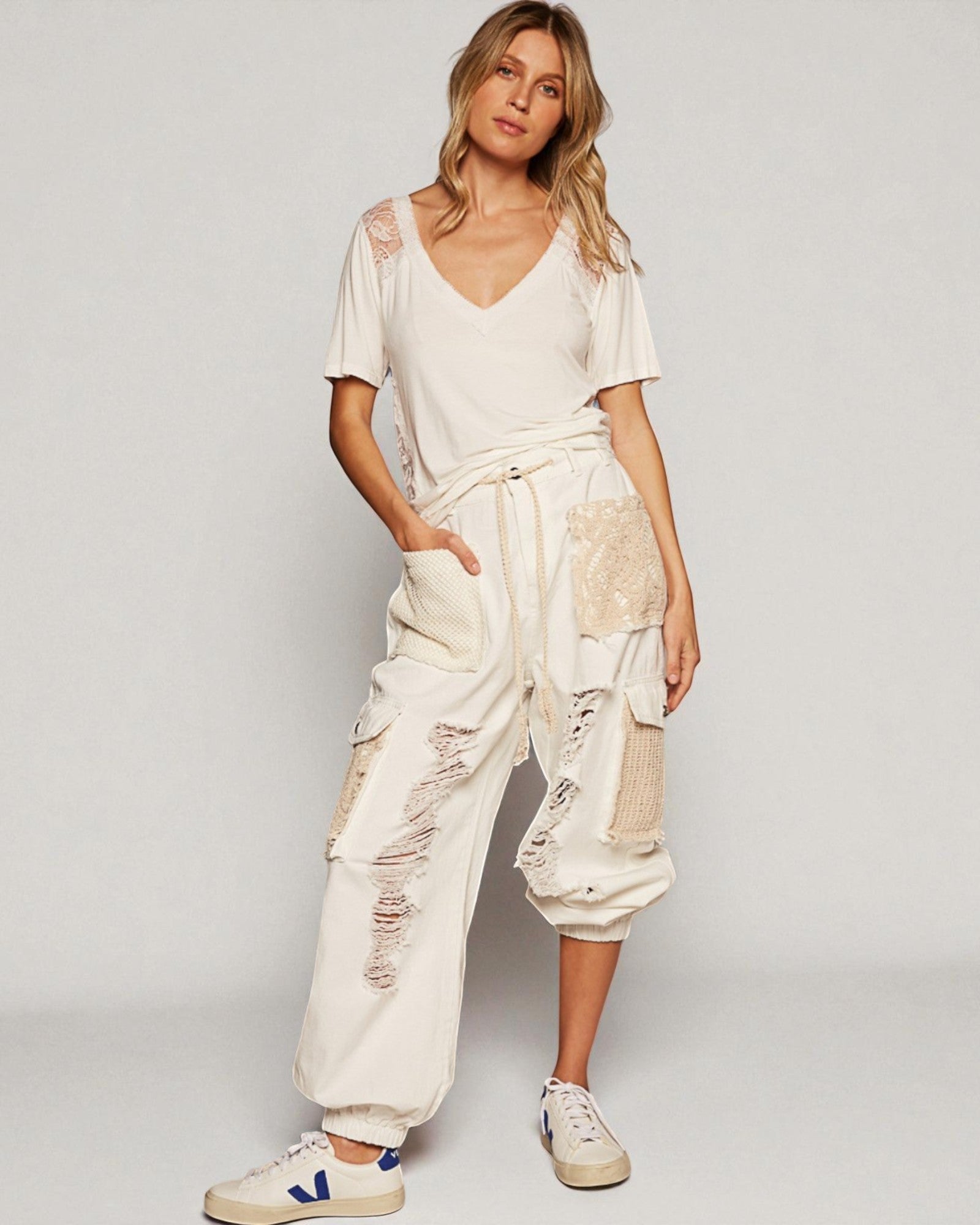 Woman wearing a white outfit with distressed details on a plain background