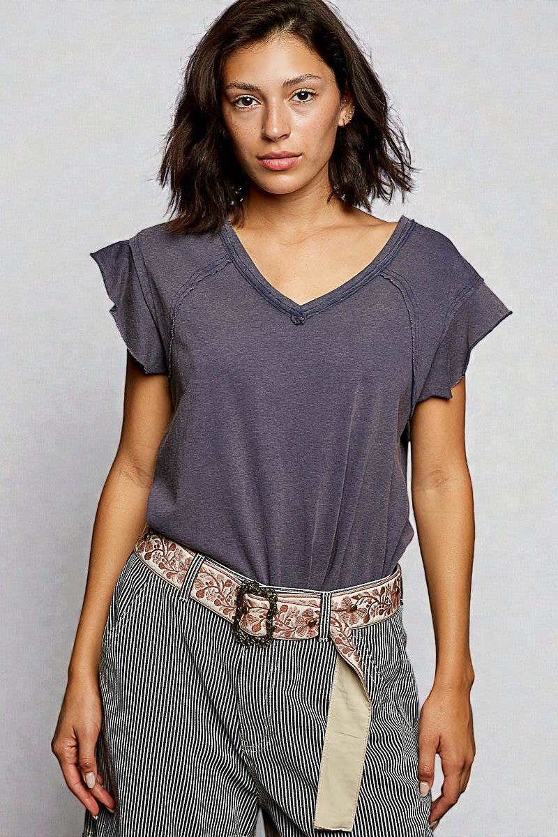 Woman wearing a purple top and striped pants with a belt against a plain background