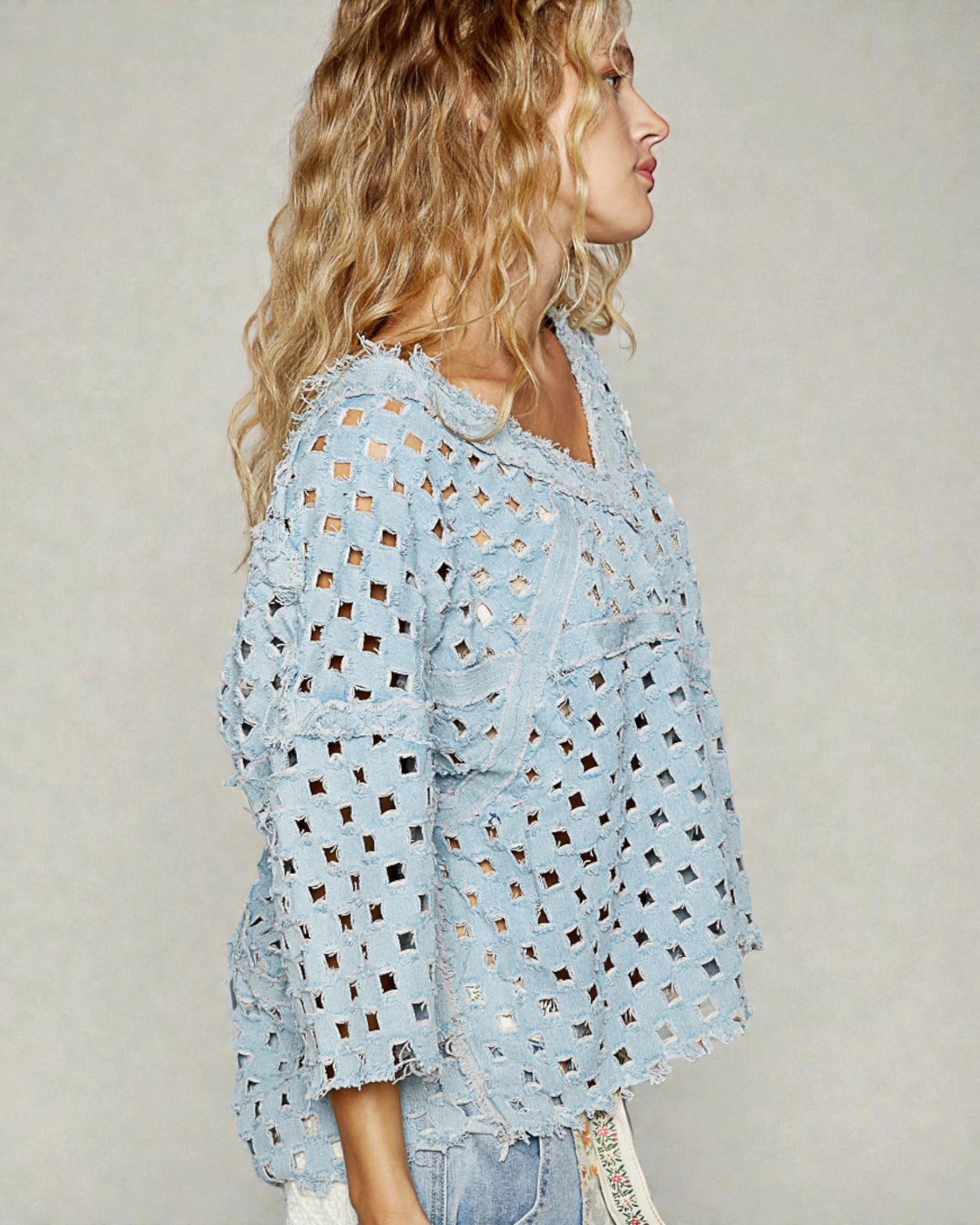 Woman wearing a light blue perforated blouse against a neutral background