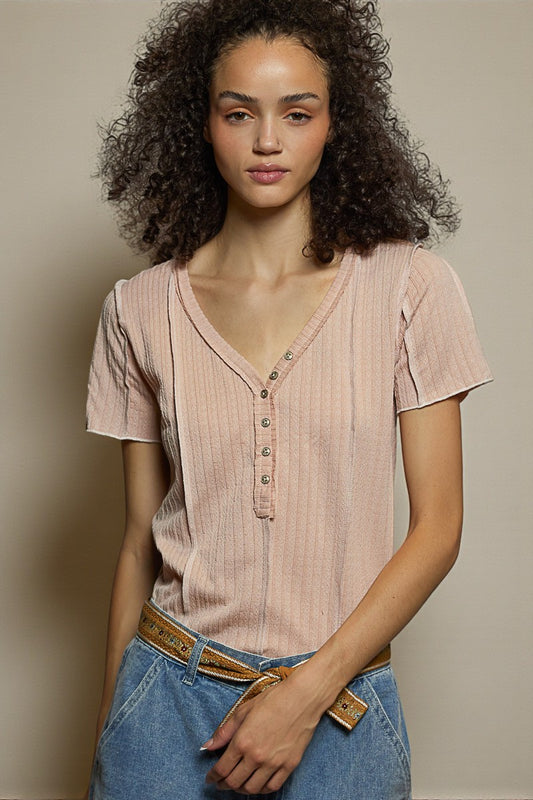 Woman wearing a light pink ribbed shirt and blue jeans against a neutral background