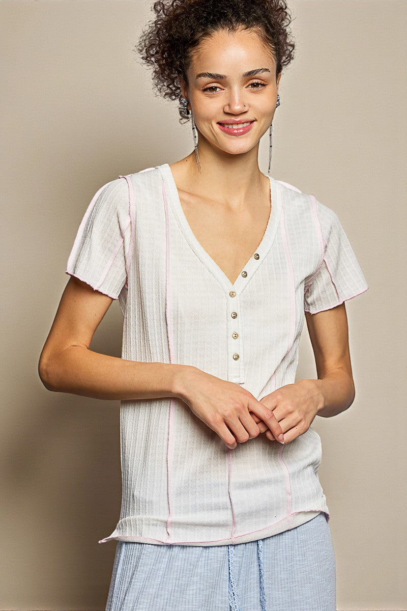 Woman wearing a light-colored blouse with buttons and light blue pants against a beige background