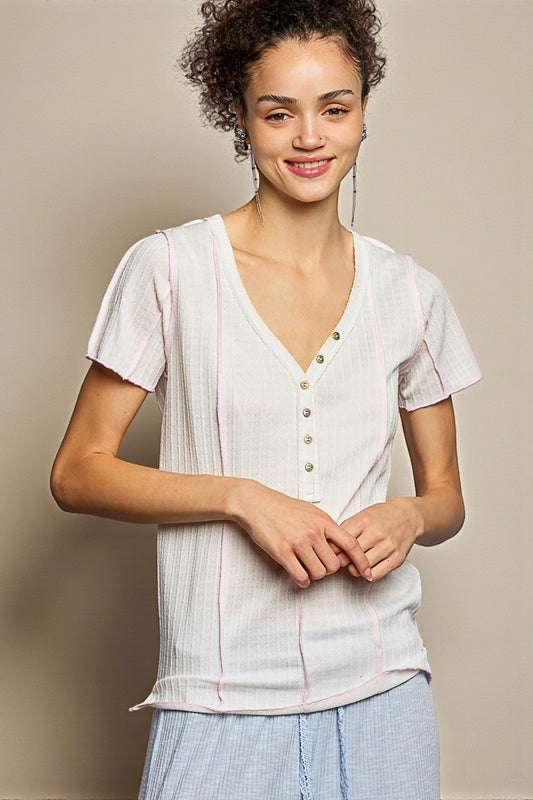 Woman wearing a light-colored blouse with buttons and light blue pants against a beige background