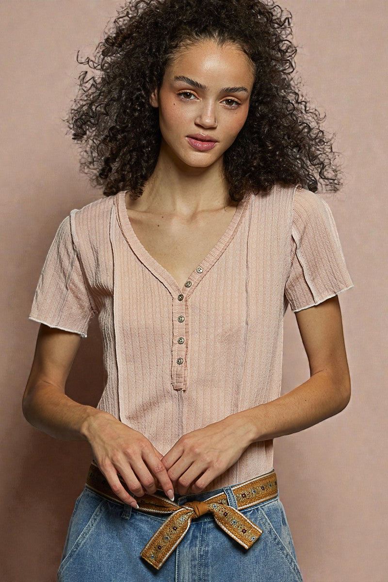 Woman wearing a light pink blouse with buttons and blue jeans against a beige background