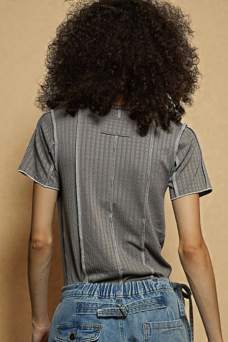 Person wearing a gray ribbed t-shirt and blue jeans against a beige background