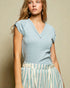 Woman wearing a light blue sleeveless top and striped skirt against a beige background