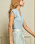 Woman wearing a light blue sleeveless top and striped pants against a neutral wall.