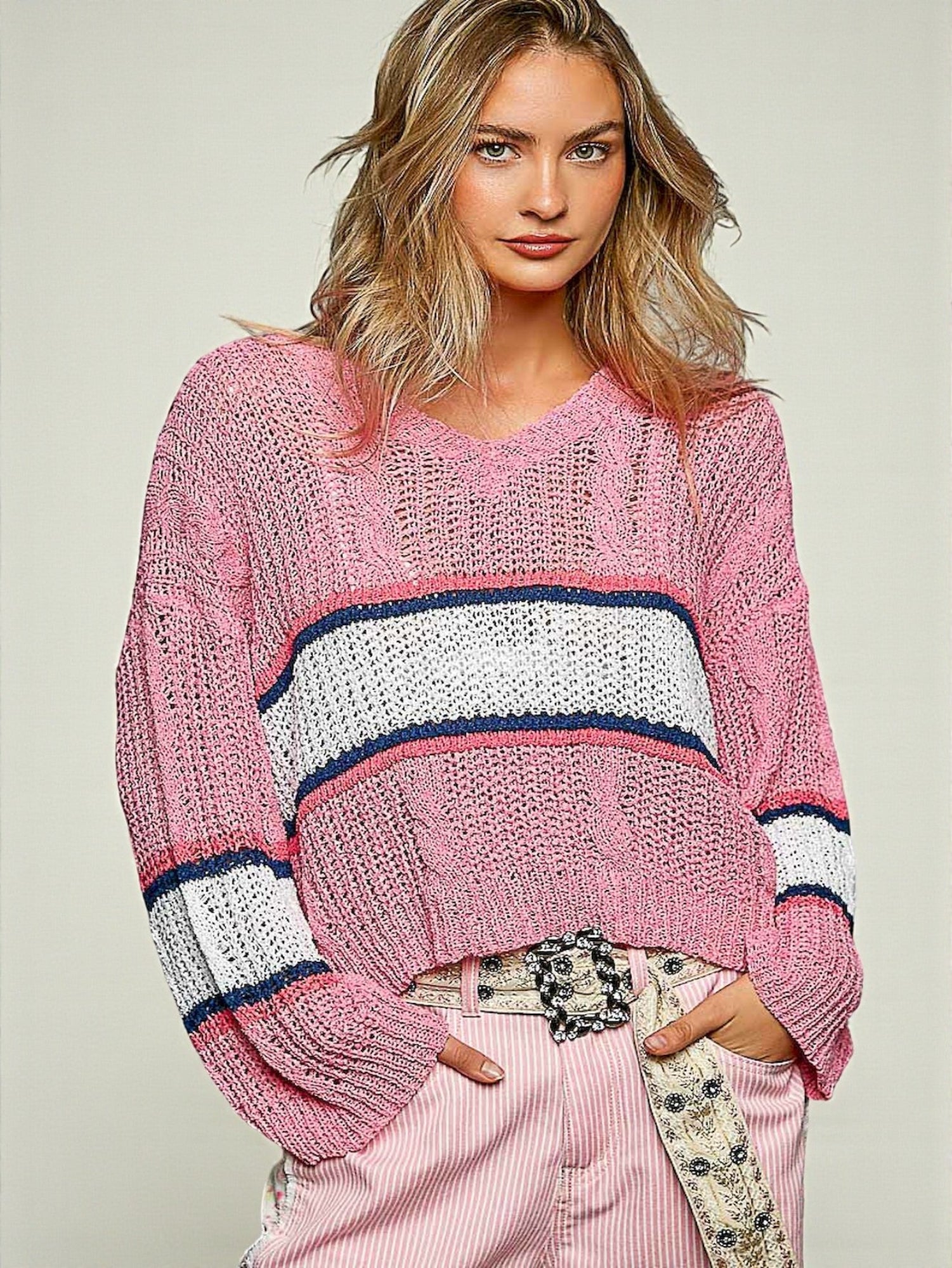 Woman wearing a pink sweater with white and navy stripes on a light background