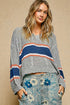 Woman wearing a gray sweater with colorful stripes and floral pants against a beige background