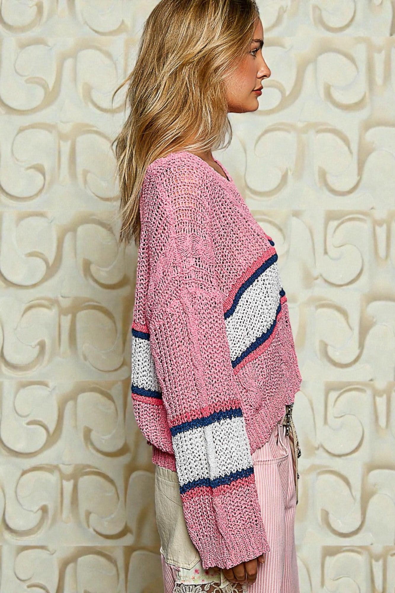 Woman wearing a pink knitted cardigan with colorful stripes against an ornate wall.