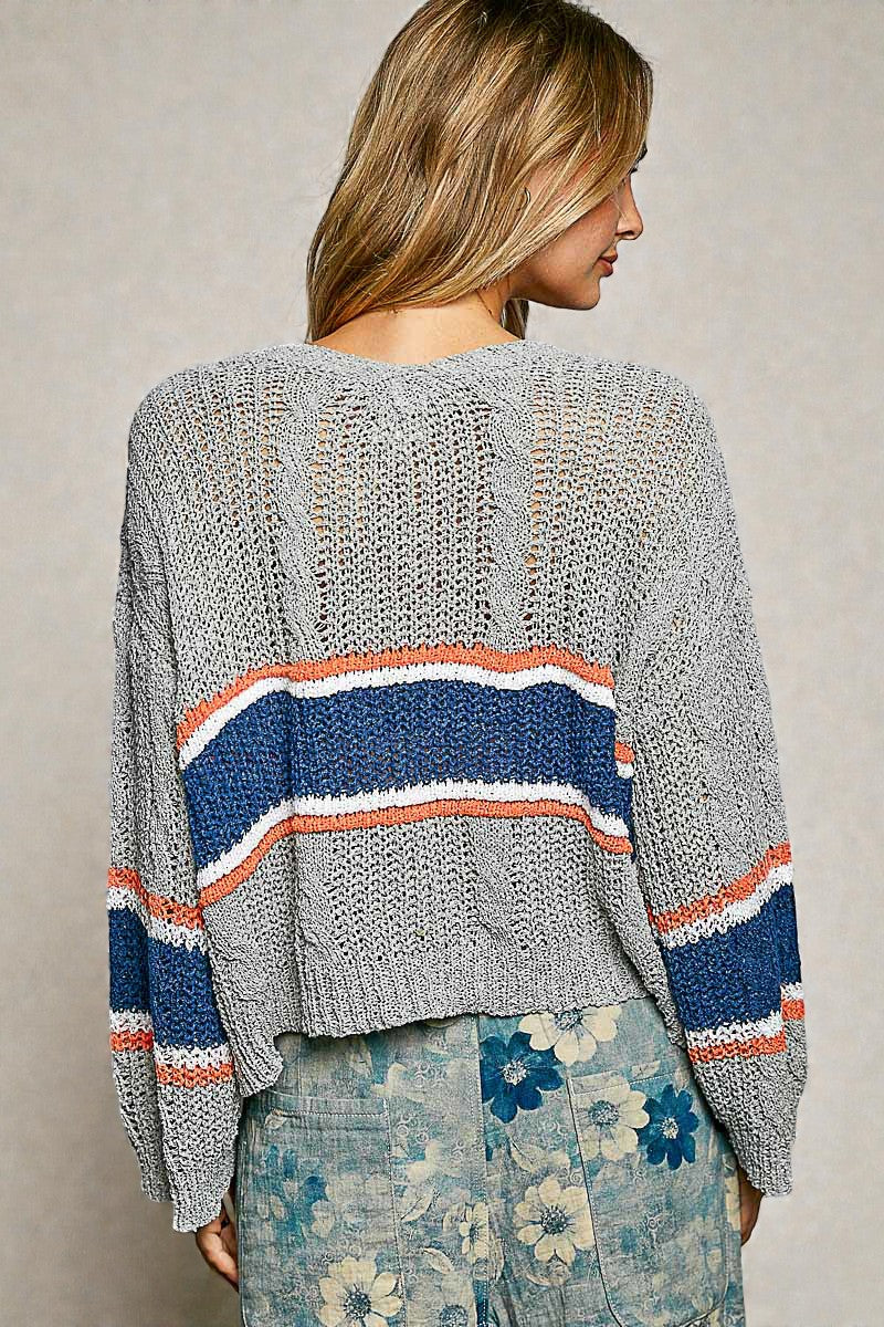 Woman wearing a gray knit sweater with colorful stripes on a neutral background