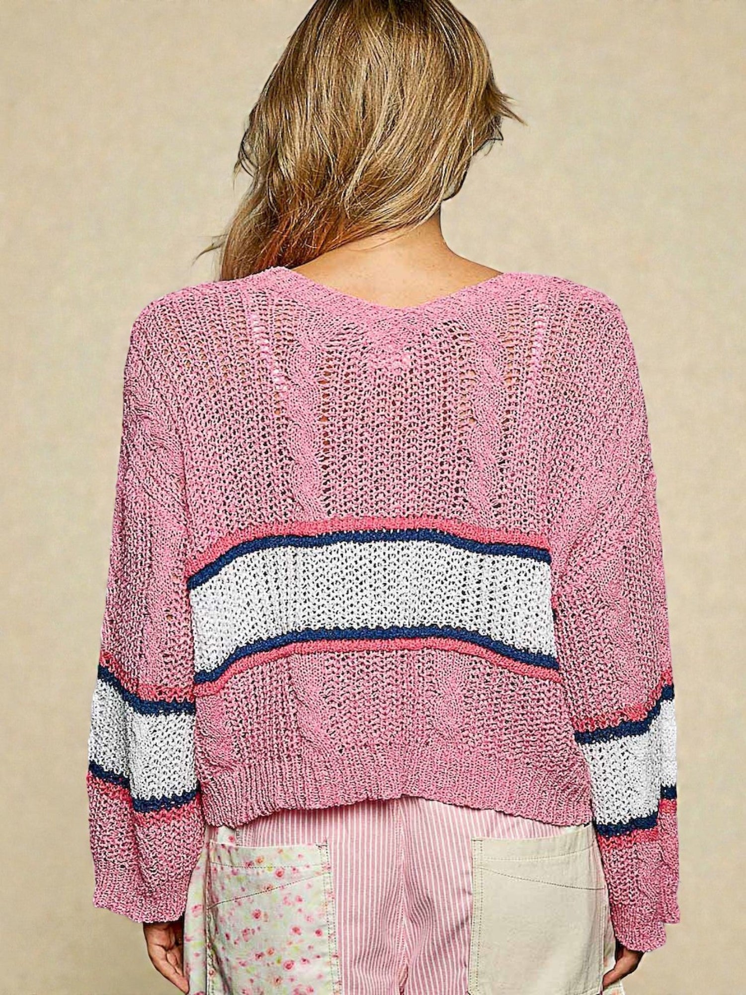 Pink knitted sweater with horizontal stripes worn by a person on a beige background