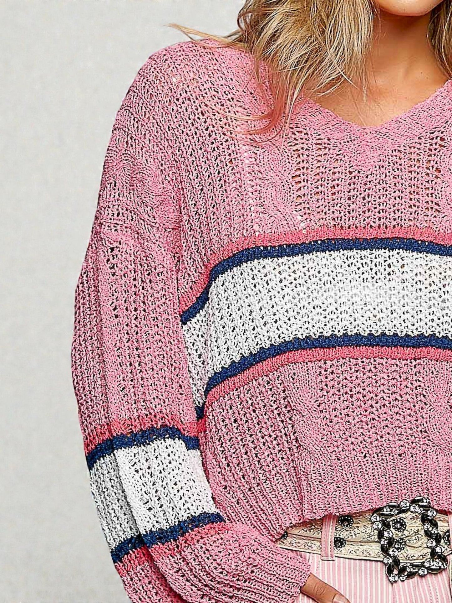 Pink knitted sweater with white and navy stripes worn by a person.
