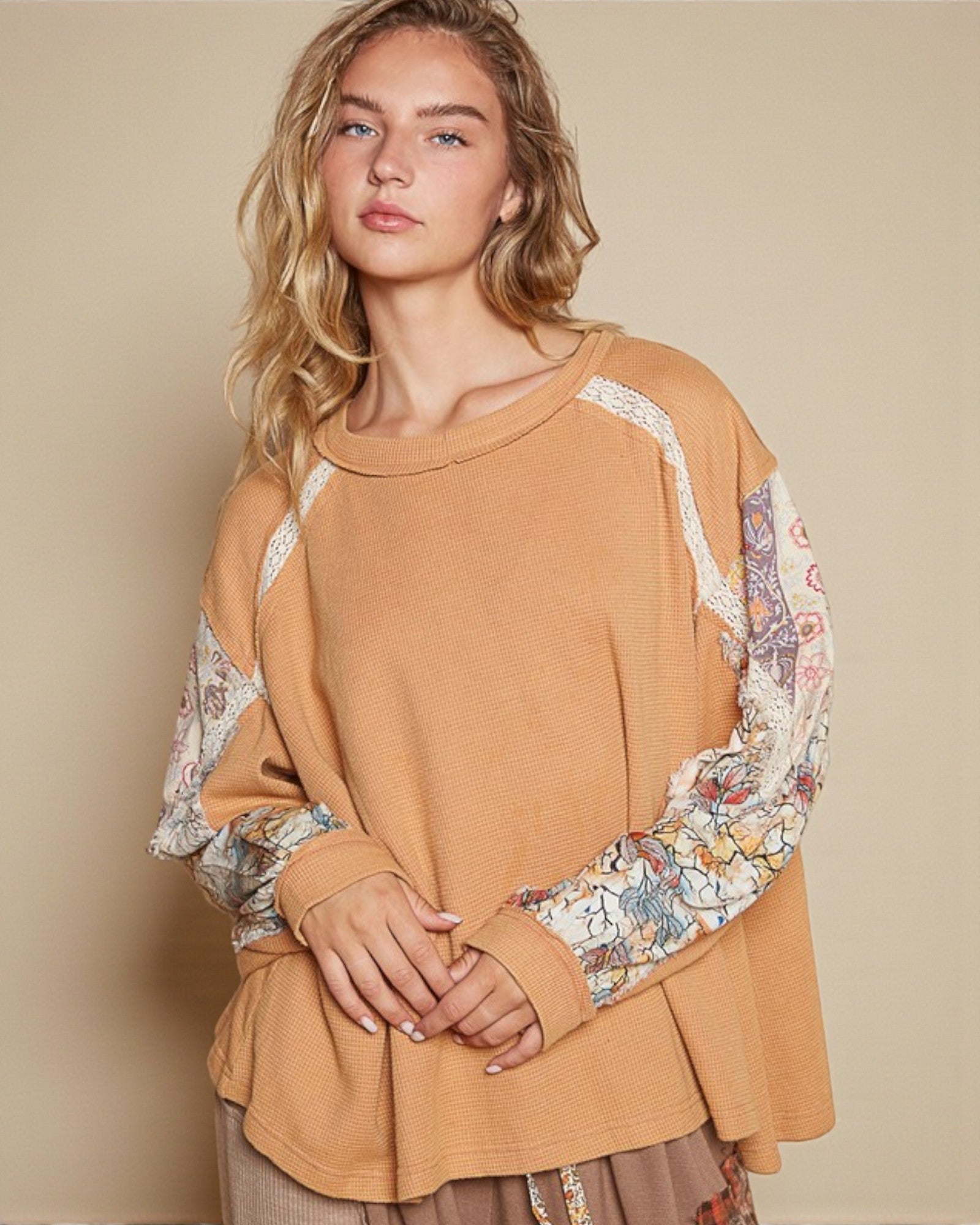 Woman wearing a mustard yellow top with floral sleeves against a beige background